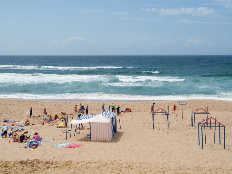 the beach has many people on it and there is an umbrella near the water