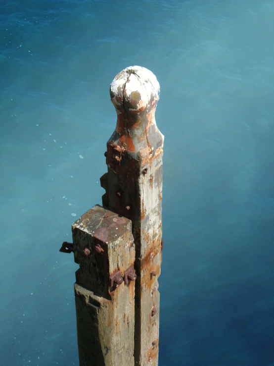 a rusted metal post standing next to the ocean