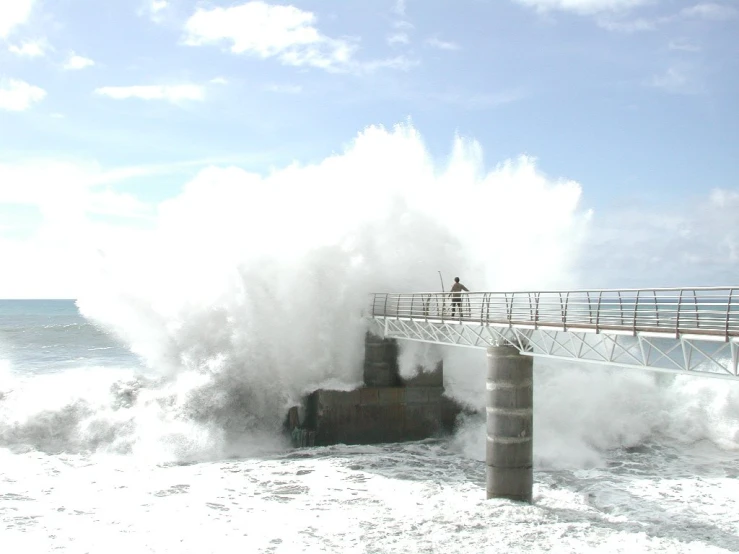 a large wave crashes while people walk under a dock