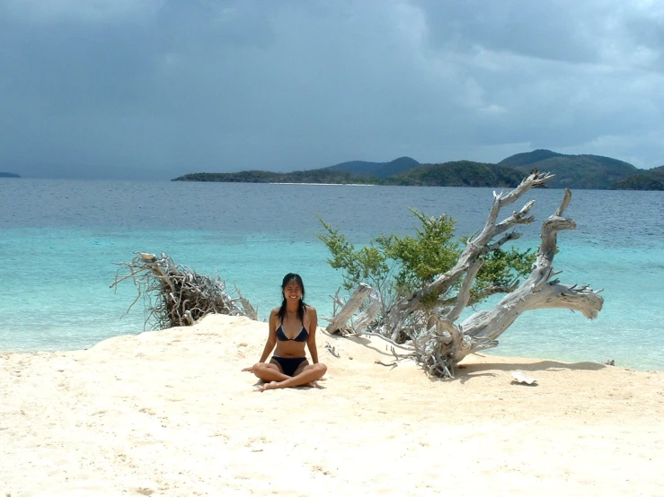 a beautiful young woman sitting on top of a sandy beach