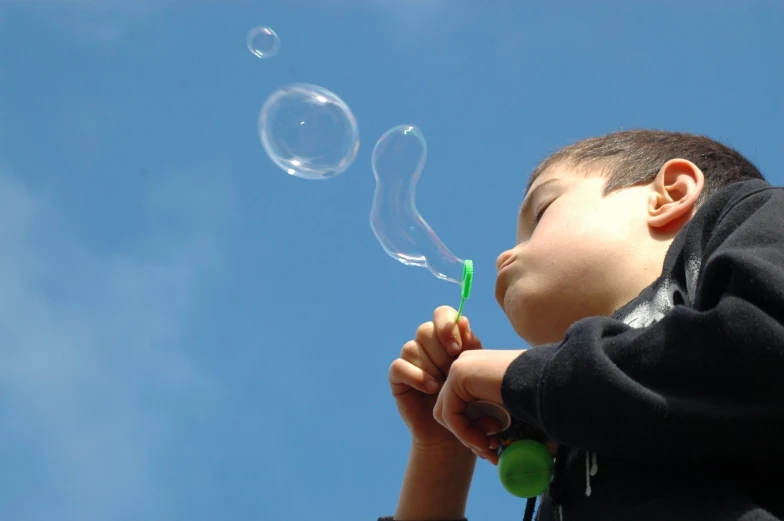 a boy blowing bubbles with one hand and another flying away