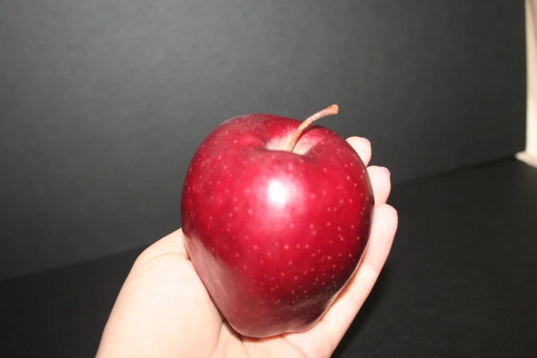 a woman's hand holding an apple against a black background