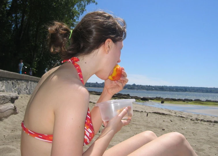 a woman with a fruit in her mouth on the beach