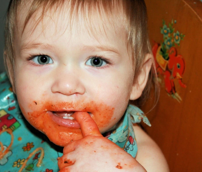 a young child is sticking out her tongue with red food on his body