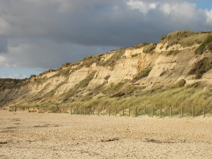 sand and grass covered hill with fencing in front of it