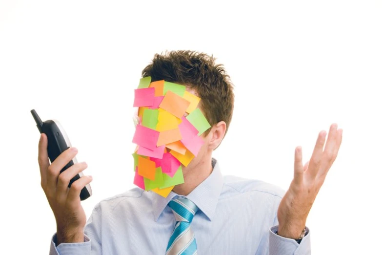 the man is holding a mobile device with post it on his face