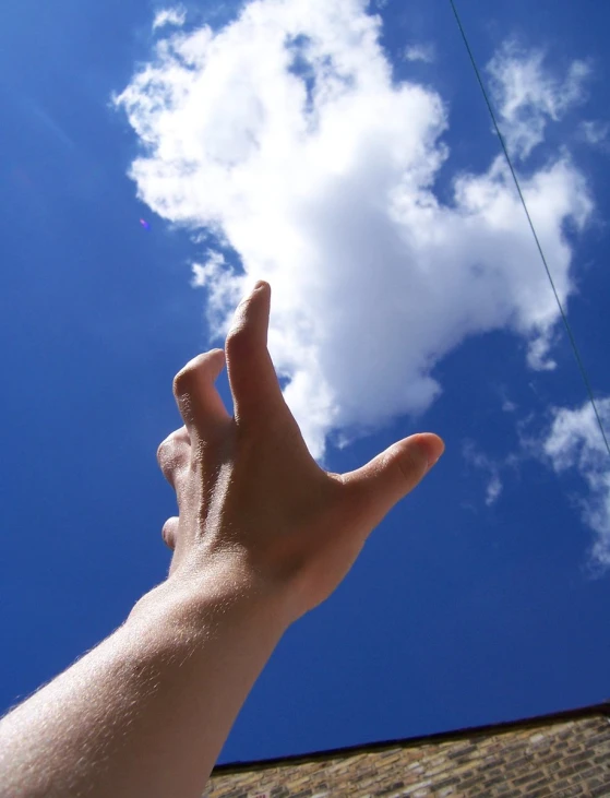 a hand with an upside down thumb is reaching up for a cloud in the sky