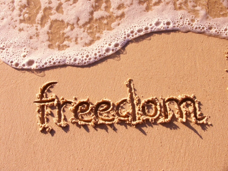 the word freedom written in sand near a wave