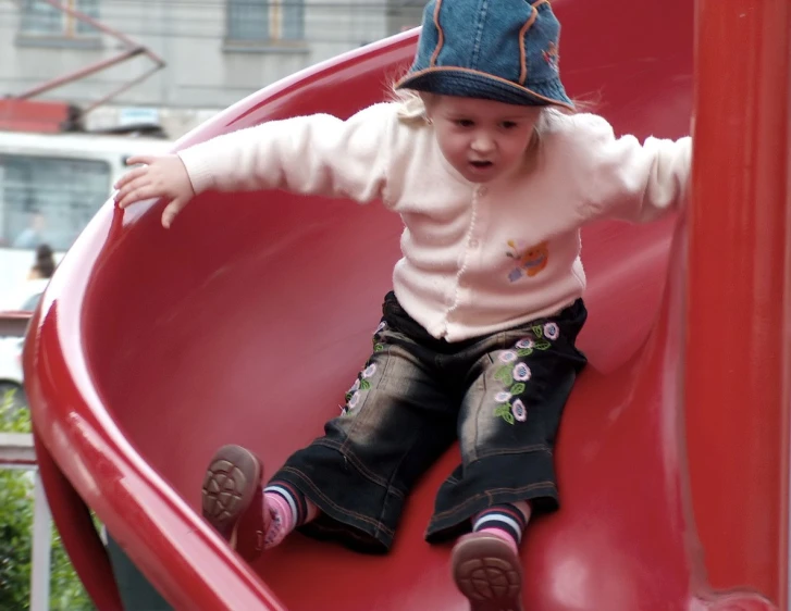 a small child wearing a hat sitting on a red slide