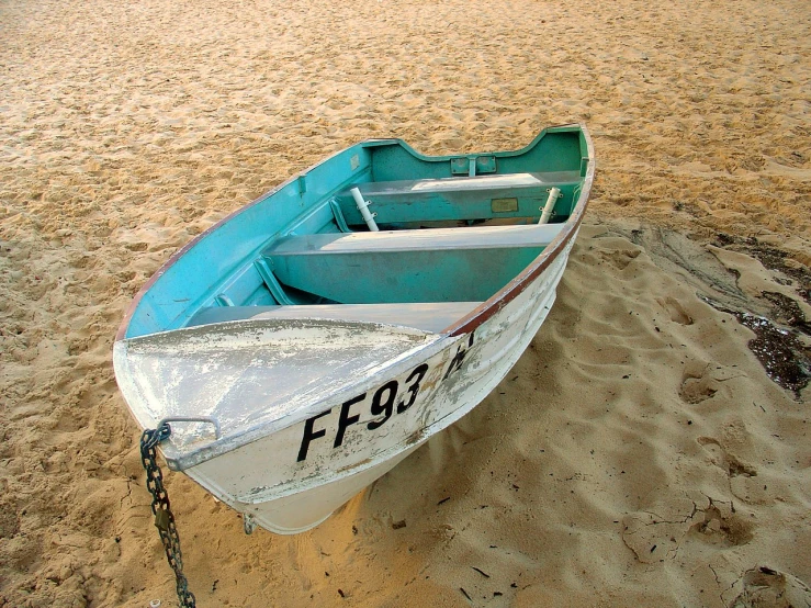 a blue and white boat with a chain on the sand