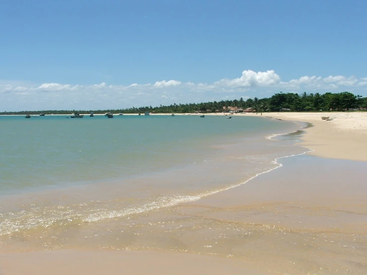 a sandy beach with blue water and several boats