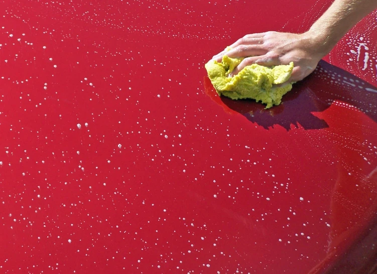 a hand on a yellow mop cleaning a car with red coating