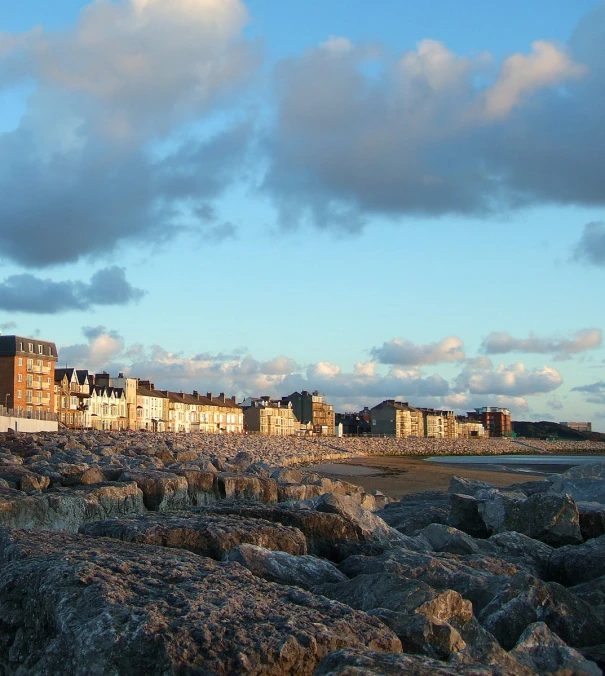 clouds gather over a beach with a row of buildings on the shore