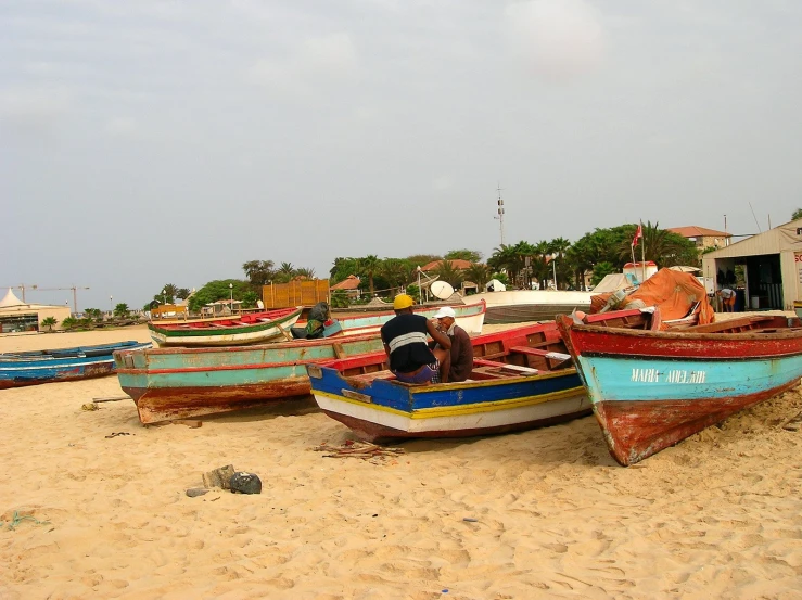 several boats laying out on the beach, with people sitting in it