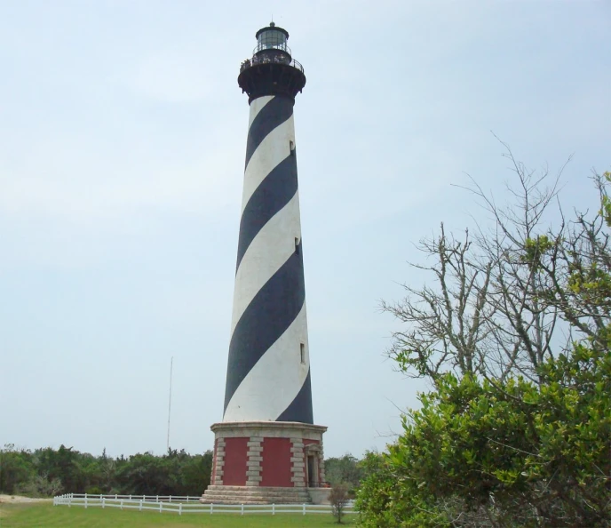 a big black and white lighthouse on top of a grass field