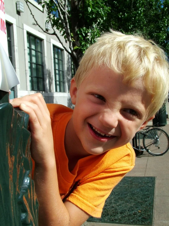 a boy in an orange shirt standing on a ledge near some street signs