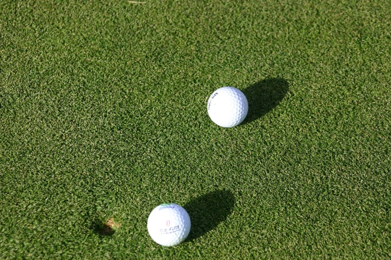 two golf balls on grass with one golf ball near the ground