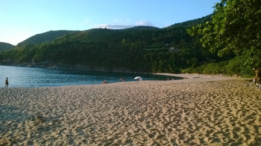 some people are laying on a beach while others stand at the water's edge