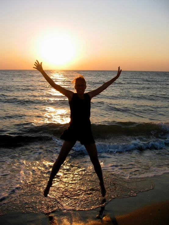 a person jumps on the beach as the sun sets