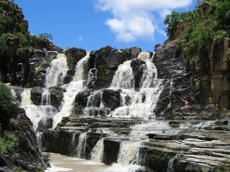 a waterfall near a man standing at the end of it