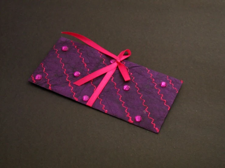 a small rectangular purple patterned piece with a pink ribbon