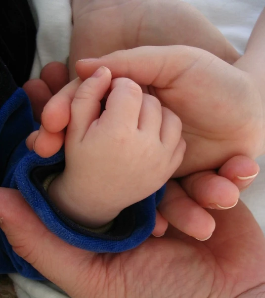 a mother holding her baby's hand with her left thumb