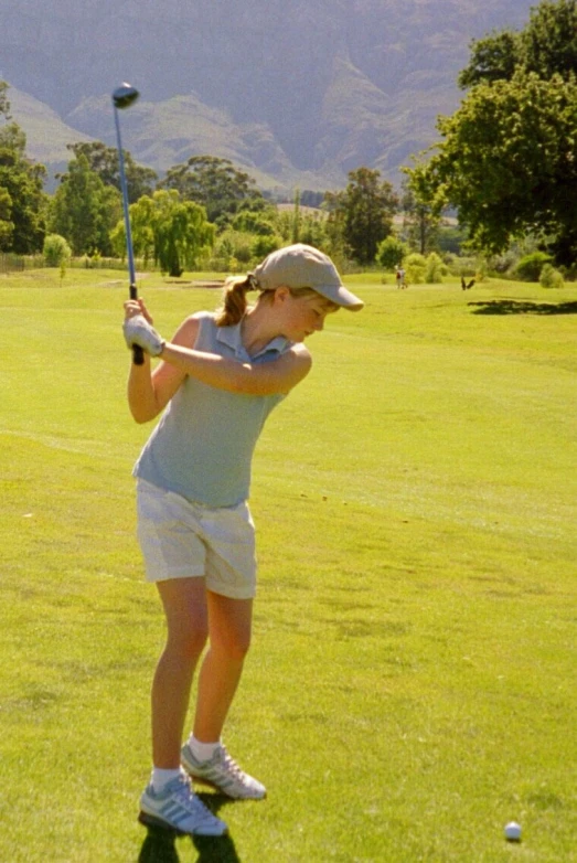 a girl in white shorts and hat hitting golf ball