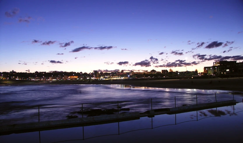 a city skyline is seen in the distance with lights reflecting off of the water