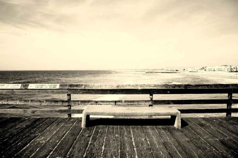 an empty bench on the end of a deck overlooking the ocean