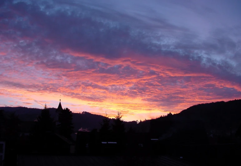 the sun sets behind a mountain range with houses