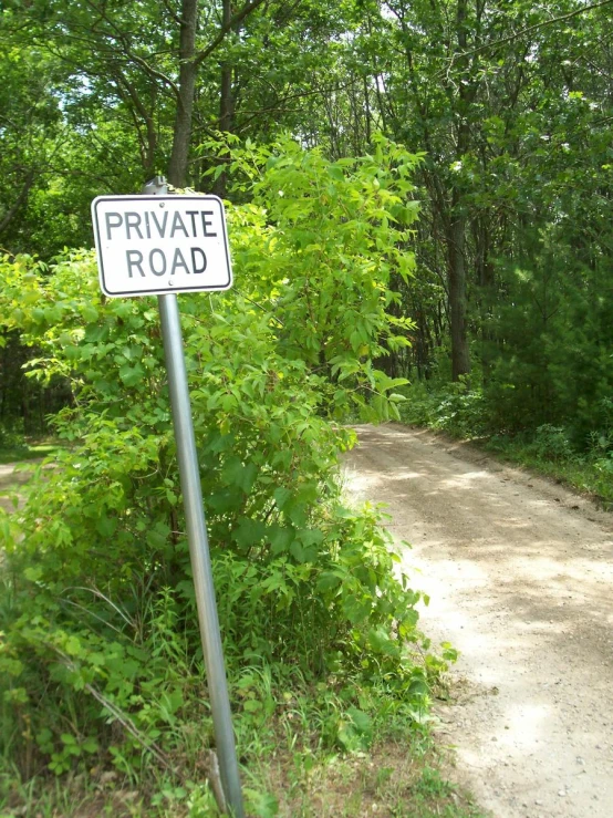 a private road sign is in the foreground while trees line the path