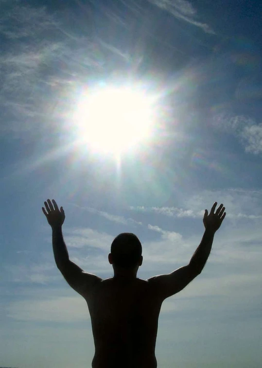 a man standing on a beach next to the ocean with his arms spread wide, in front of a bright blue sky