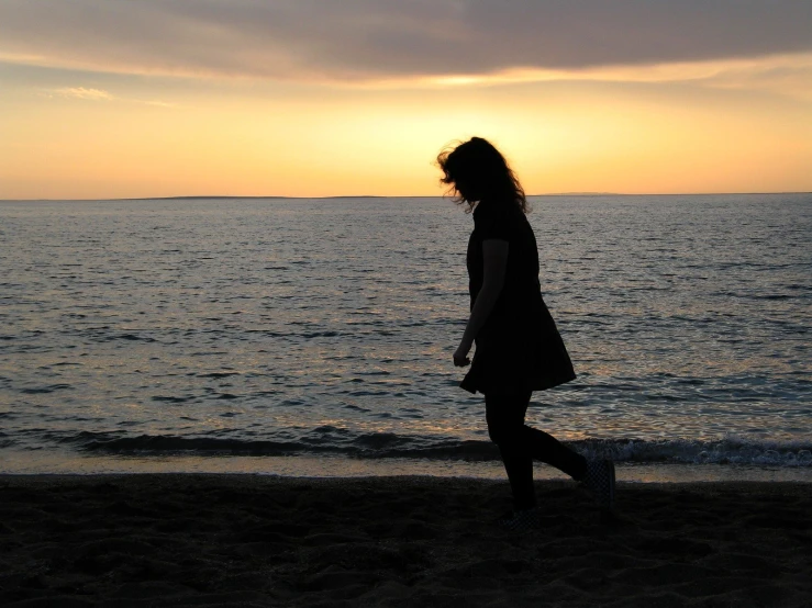 a woman walking on the beach while the sun sets