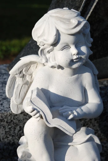 an old statue of a little angel reading a book