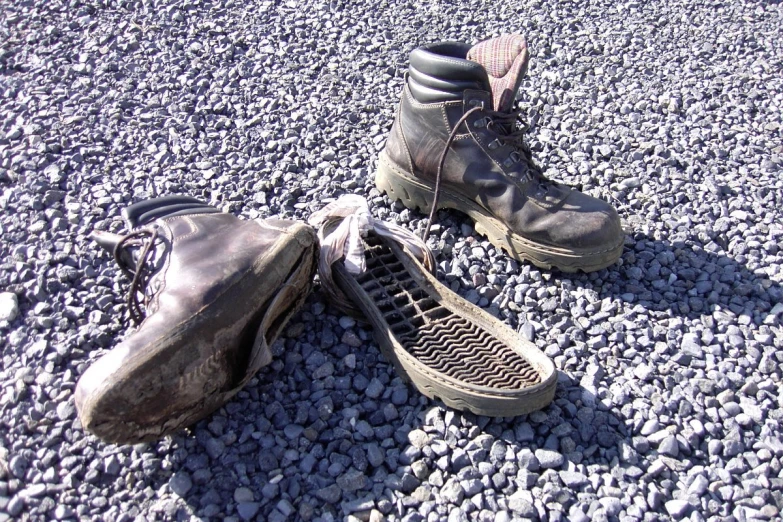 two worn sneakers, one black and one brown, are sitting on gravel