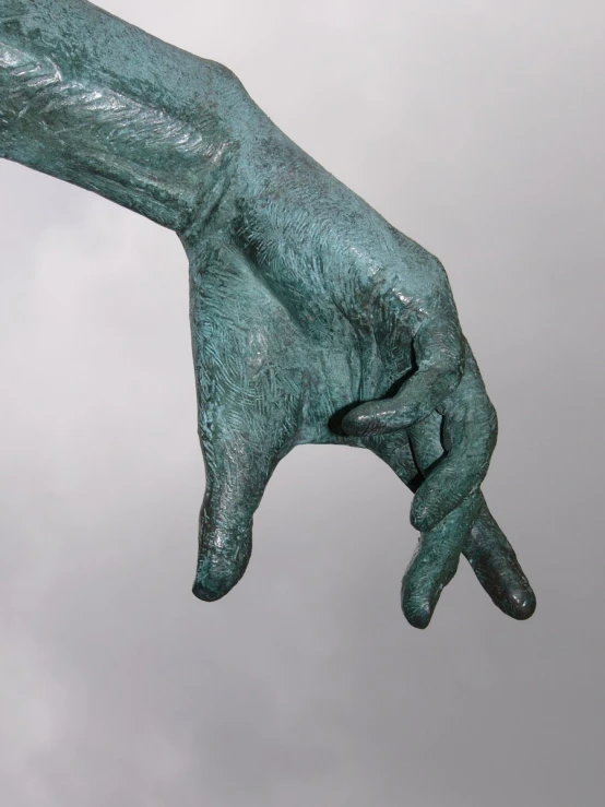 a large bronze object with the hands pointing upwards in front of a cloudy sky