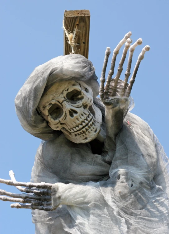 a skeleton statue has his hands up in the air with a cross above it