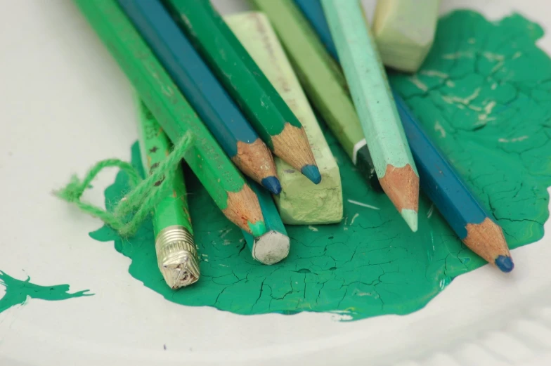 colored pencils resting on a paper plate next to green paint