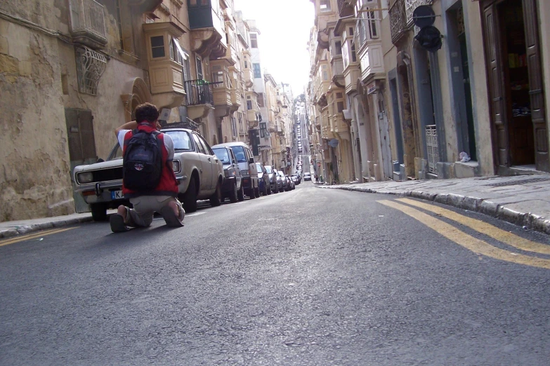 a man sitting on the street with cars behind him