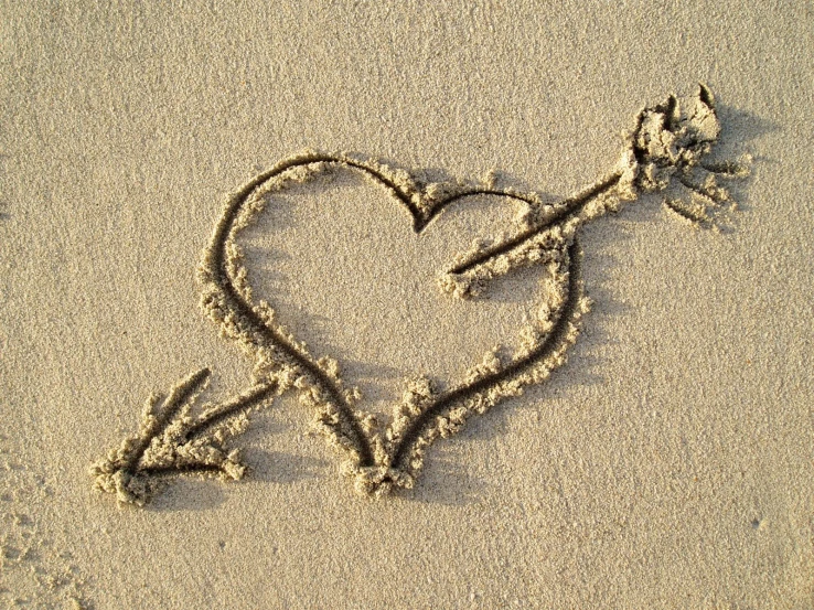 a heart and arrow made out of sand on the beach