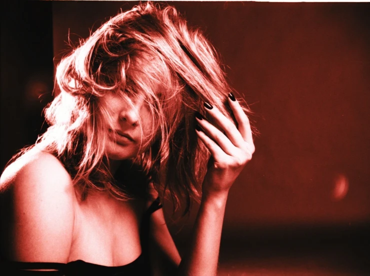 a young woman standing in a dark room holding her hand to her hair