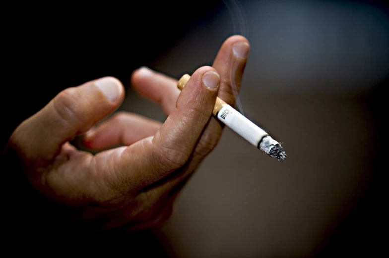 a man is holding a cigarette while wearing a yellow ring