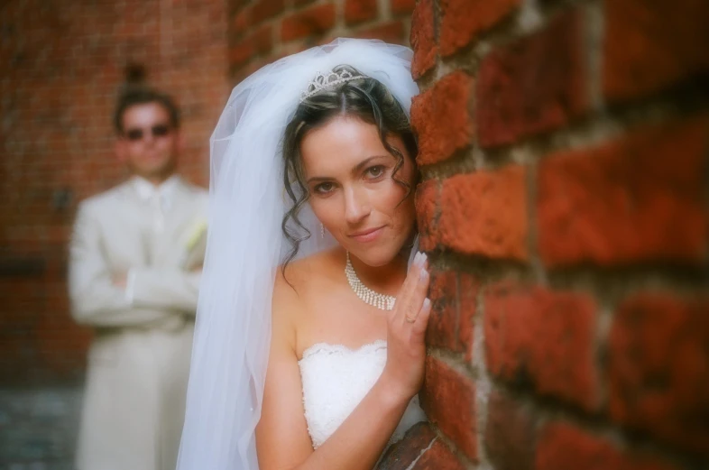 a bride is peeking against a brick wall