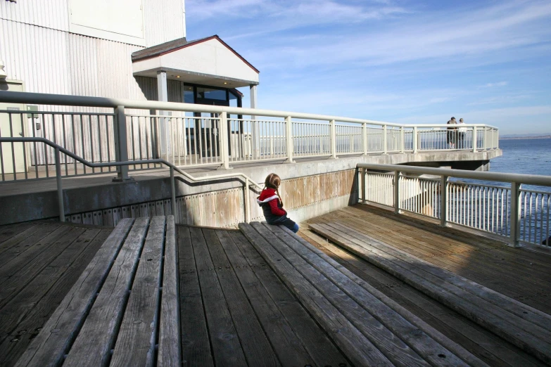 a child sitting on a wooden porch on a boardwalk overlooking water