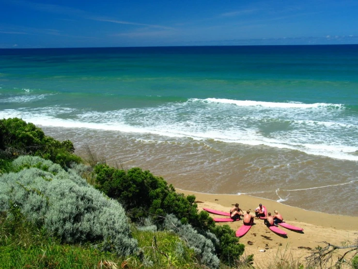 three people lay on surfboards next to the ocean