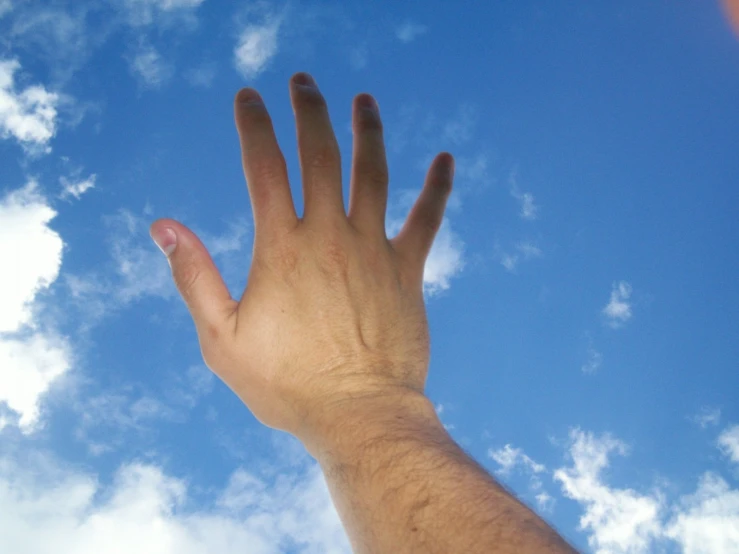 a hand reaching into a bright blue sky with clouds