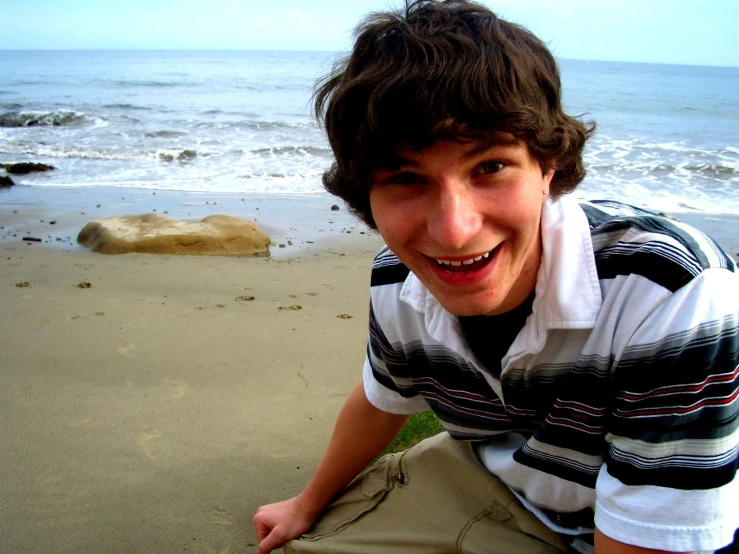 a man smiling next to the ocean on a beach