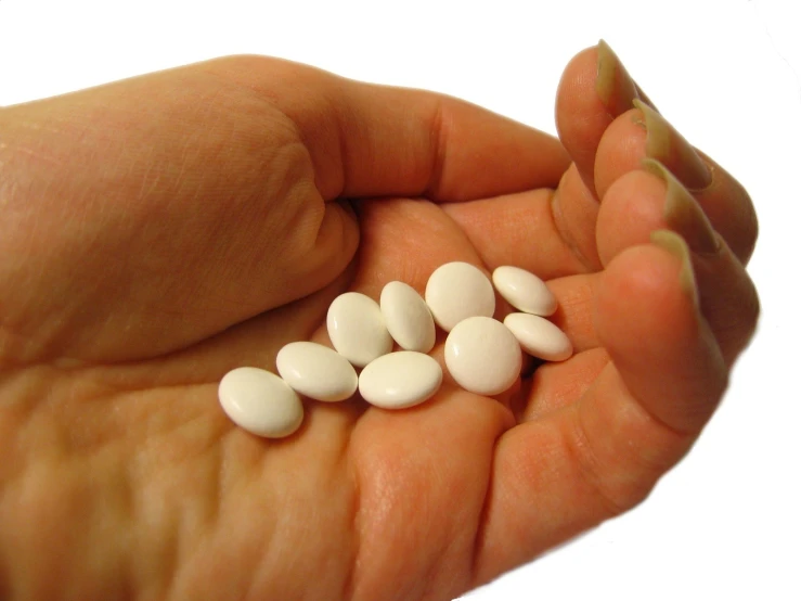 the person is holding several white pills in their hand