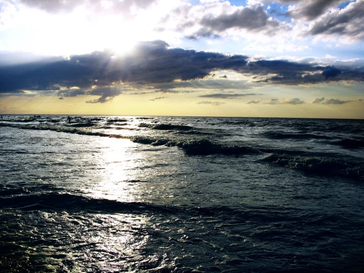 a person stands in the ocean near the shore under the cloudy sky