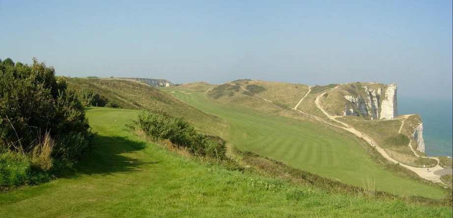 a large grassy field with a golf course near the ocean